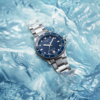 A silver wristwatch with a blue dial on icy surface.