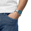 Person wearing blue jeans and a wristwatch with hand in pocket.