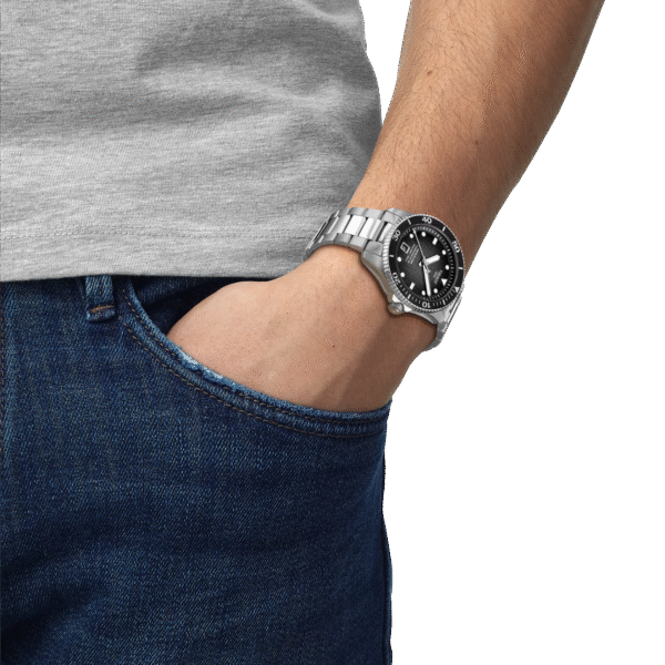 Man wearing a silver wristwatch with hand in jeans pocket.