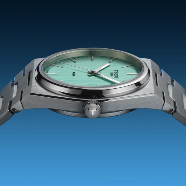 Close-up of a silver wristwatch with a mint green face against a blue background.
