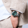 A stylish man wearing a beige suit and a green-faced wristwatch.