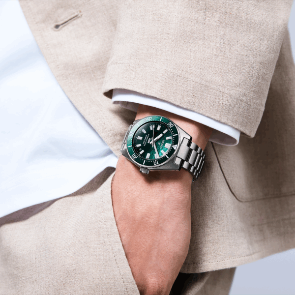 A stylish man wearing a beige suit and a green-faced wristwatch.