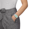 Woman wearing a mint green wristwatch with grey pants and white top.